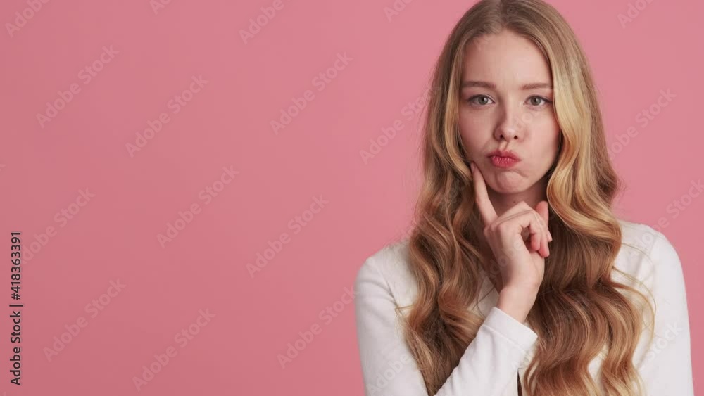 A happy young woman is thinking about something and coming-up with an idea while raising up her finger standing isolated over pink wall in the studio A happy young woman is thinking about something and coming-up with an idea while raising up her finger standing isolated over pink wall in the studio