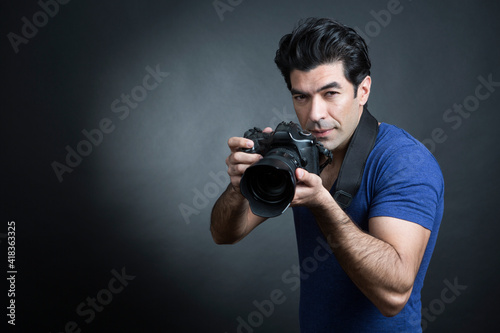 fotografo moro in maglietta blu e fotocamera al collo è pronto a fare una foto  , isolato su sfondo nero