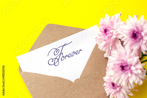 Love envelope and letter with written word forever with pink chrysanthemum flowers on bright yellow bacground.