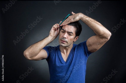 uomo moro in maglietta blu si pettina i capelli con espressione sicura di se, isolato su sfondo nero photo