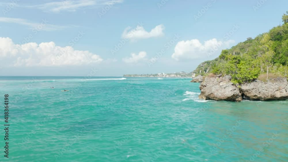 Low aerial view of surfers in tropical blue ocean by steep cliffs with luxury villas in Bali, Indonesia Low aerial view of surfers in tropical blue ocean by steep cliffs with luxury villas in Bali, Indonesia