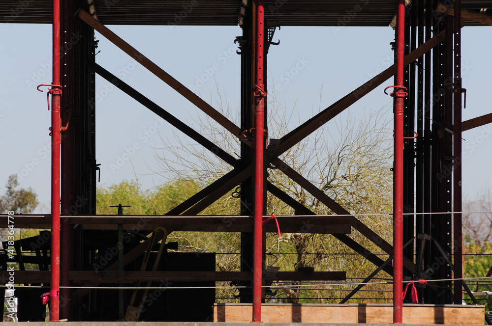 Structural steel framing with red support columns and diagonal bracing at construction site, illustrating mixed-use building infrastructure during early development phase Structural steel framing with red support columns and diagonal bracing at construction site, illustrating mixed-use building infrastructure during early development phase