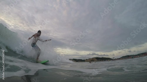 Single fit active young latin Tourist man surfing over a turquoise blue emerald deep Pacific Ocean, wearing a surfer boardshort, waiting a ocean wave during the sunset time at Canoa, Manabi, Ecuador.