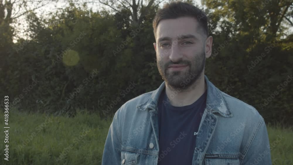 Male wearing denim jacket smiling at camera, located outside in the green countryside. Male wearing denim jacket smiling at camera, located outside in the green countryside.