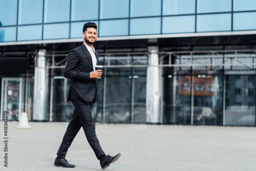 Smiling happy Indian goes to work in the office, behind him a modern building, a modern Indian man, a businessman Smiling happy Indian goes to work in the office, behind him a modern building, a modern Indian man, a businessman
