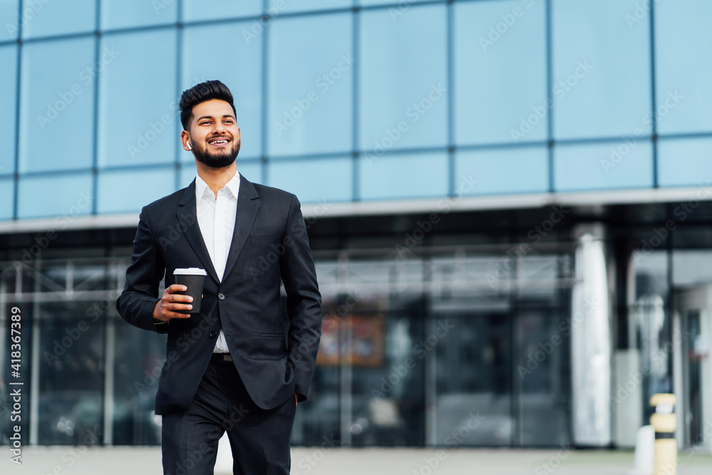 Successful and happy Indian man, businessman, smiling happily going to a business meeting, behind him a modern office building Successful and happy Indian man, businessman, smiling happily going to a business meeting, behind him a modern office building