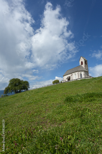 St. Giacomo little church among a wide green meadow in St. Giacomo town , Val di Funes