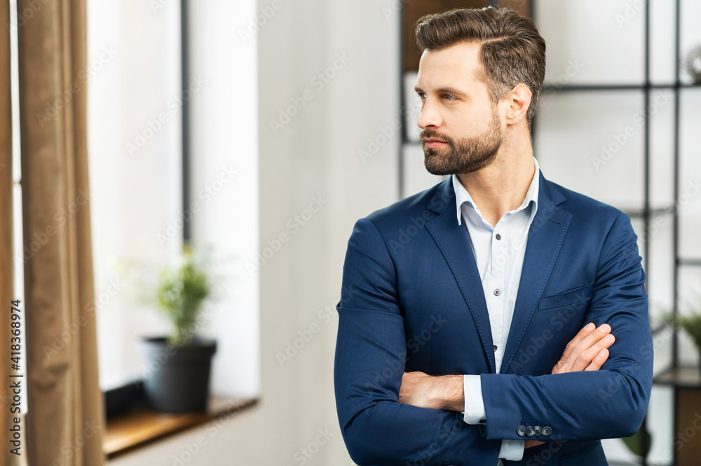 Portrait of a successful businessman with neat bristles, standing arms crossed, looking to the side, dressed in an expensive blue suit, elegant male model look in distance, side profile image Portrait of a successful businessman with neat bristles, standing arms crossed, looking to the side, dressed in an expensive blue suit, elegant male model look in distance, side profile image