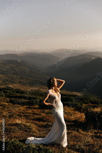 Beautiful bride in a white wedding dress silhouetted from the rays of the sun, on a background of mountains