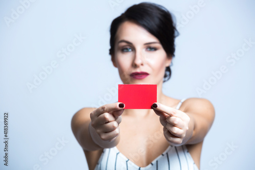 Donna bianca con i capelli neri vestita con una tuta bianca a righe mostra una card rossa , isolata su sfondo bianco