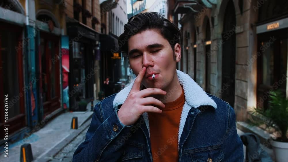 A young pretentious man smoking on the narrow street