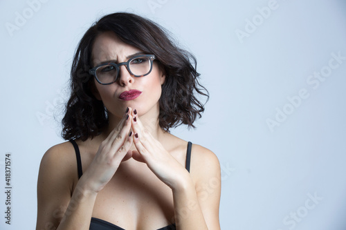 Ritratto di ragazza bianca con i capelli mori e con occhiali da vista prega in segno di disapprovazione , isolata su sfondo bianco