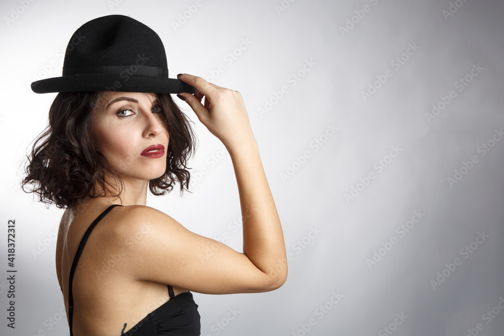 Bellissima ragazza mora con un abito nero e cappello nero posa isolata su sfondo bianco. Bellissima ragazza mora con un abito nero e cappello nero posa isolata su sfondo bianco.