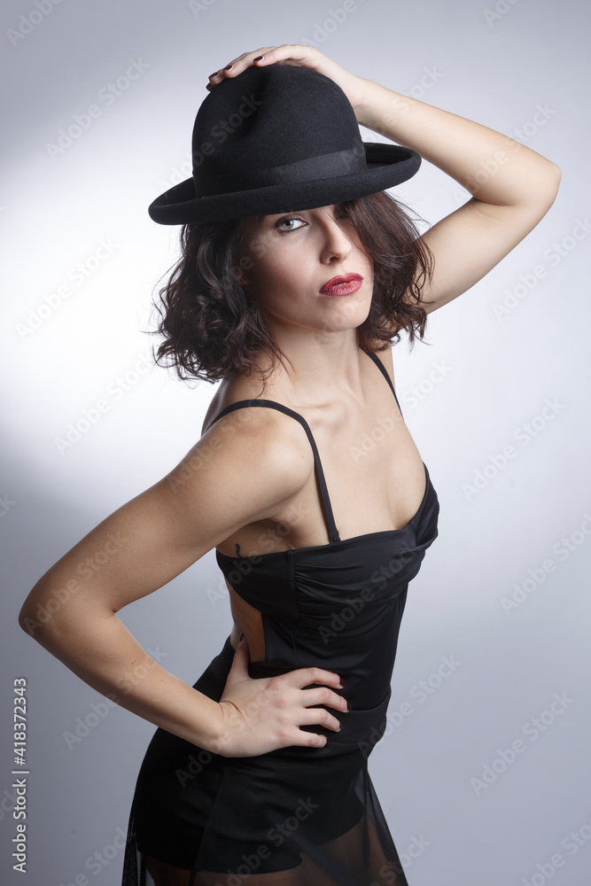 Bellissima ragazza mora con un abito nero e cappello nero posa isolata su sfondo bianco. Bellissima ragazza mora con un abito nero e cappello nero posa isolata su sfondo bianco.