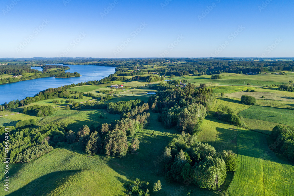 A large lake with blue water surrounded by numerous hills, forests and fields on the landscape from a drone.
