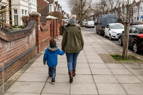 A mother and son walking on the pavement holding hands shot from behind