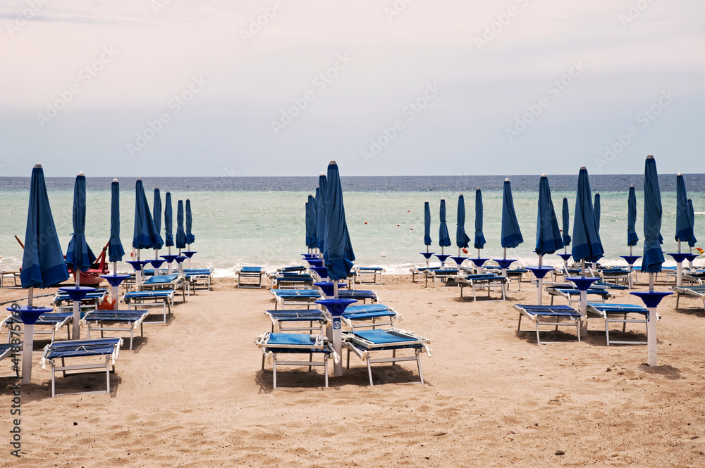 Typical Italian lido on a sandy beach with umbrellas and sunbeds closed in the evening in front of the horizon. 