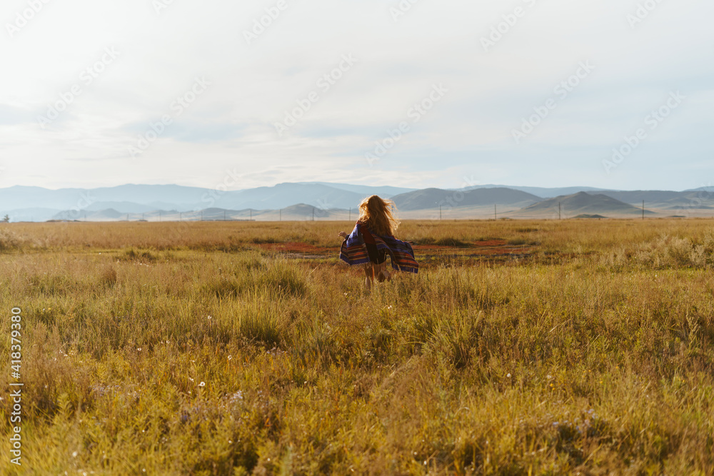 far away on the steppe grass towards the hills runs barefoot girl with a cape on her shoulders. High quality photo