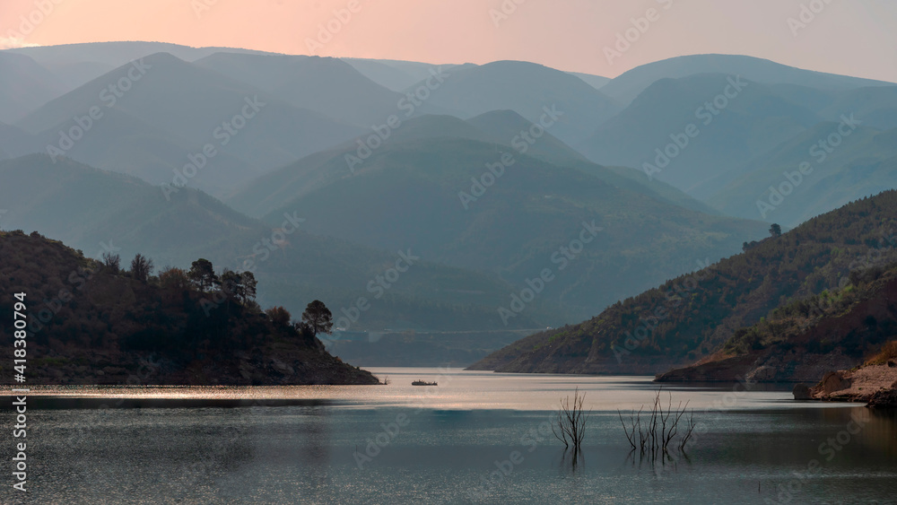 Landscape of a reservoir surrounded by large mountains blurred by mist.