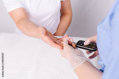 Crop image of female doctor measuring glucose level blood test with digital glucometer and small drop of bloo. Diabetes patient on a white hospital background with side empty space for advertisement