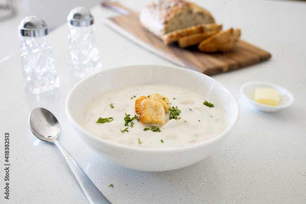 Bowl of Clam Chowder with Whole Grain Bread on a White Kitchen Counter Bowl of Clam Chowder with Whole Grain Bread on a White Kitchen Counter