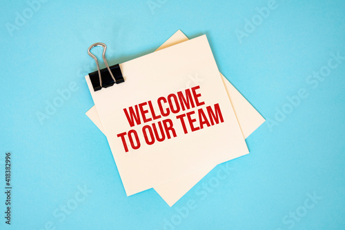 Text WELCOME TO OUR TEAM on sticky notes with copy space and paper clip isolated on red background.Finance and economics concept.
