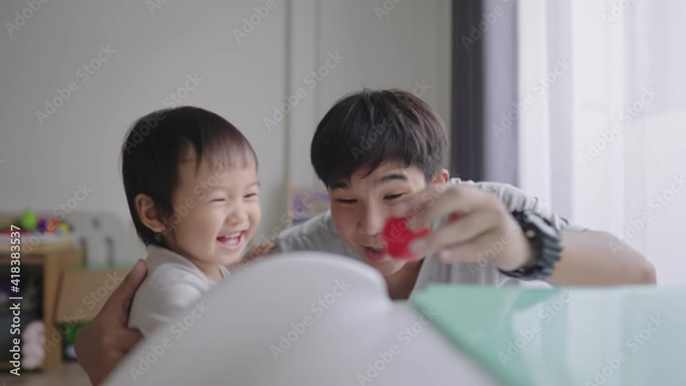 Playful family playing with each other during a day at home, Young cheerful father convinces her daughter to play with him by showing a red ball on slider next to white curtain in day time, together Playful family playing with each other during a day at home, Young cheerful father convinces her daughter to play with him by showing a red ball on slider next to white curtain in day time, together