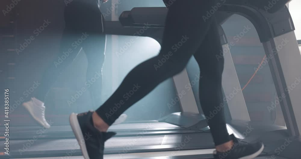 Woman and man running on treadmill at the gym. Below view of athletic people, slow motion