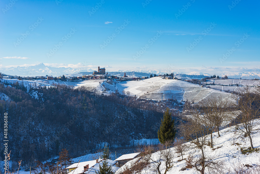 Italy Piedmont: row of wine yards, unique landscape in winter with snow, rural village on hill top, italian historical heritage nebbiolo grape agriculture