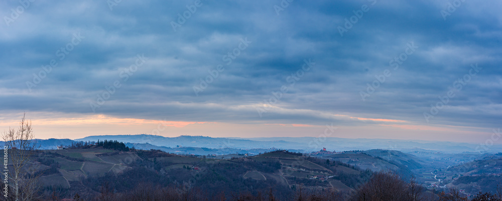 Italy Piedmont: panoramic winter snow view wine yards unique landscape at sunset, medieval castle and village on hill top, the Alps in the background dramatic sky