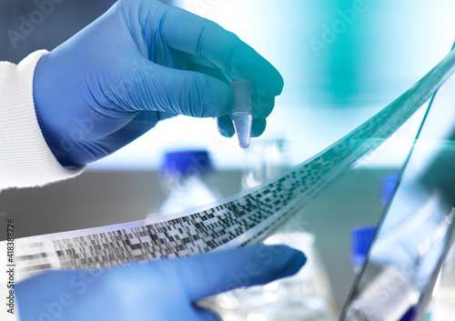 Research scientist holding a sample in a vial with DNA results on autoradiogram gel in laboratory, close up of hand photo