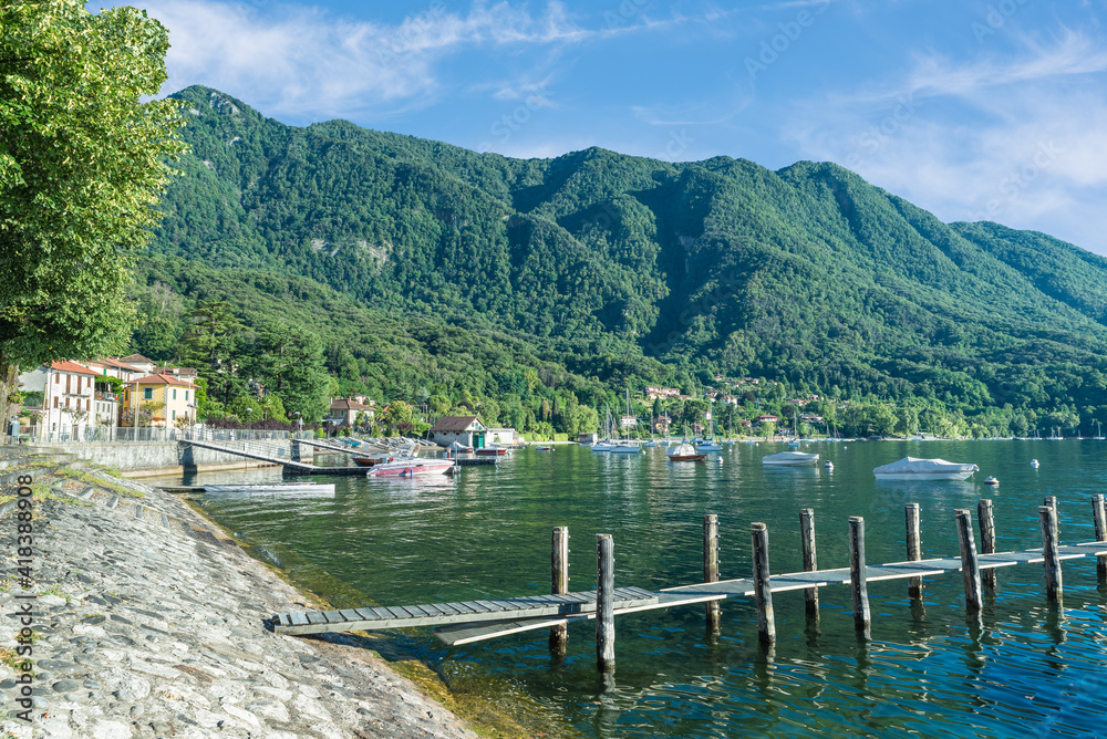 Fototapeta premium Fascinating glimpse of a large Italian lake with moored boats and a jetty in the foreground. Lake Maggiore at the village of Caldè (Castelveccana), northern Italy 