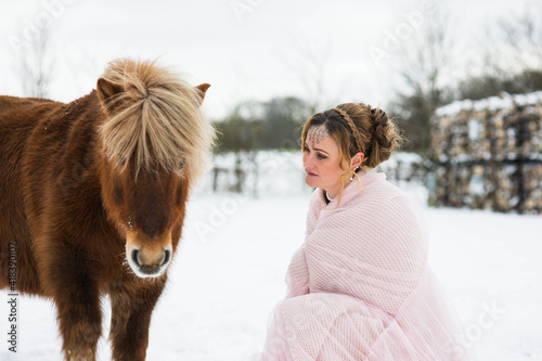 Eine wunderschöne Frau im Rosa Tüll Kleid, sieht aus wie Aschenputtel, steht im Schnee und schauet ihren Pferd liebevoll an