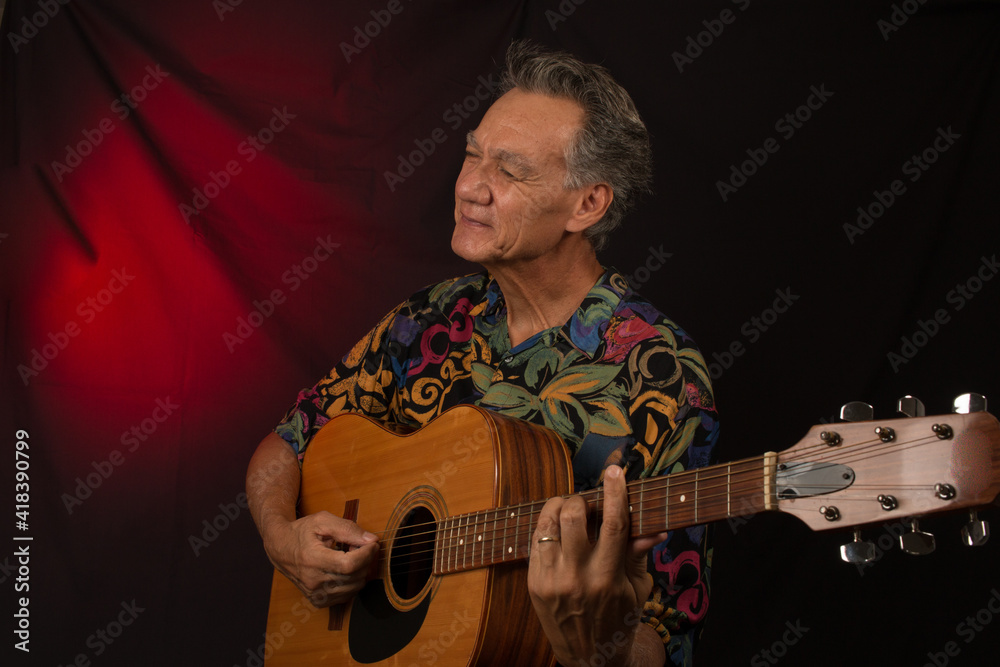 Obraz premium Older Man having fun playing his acoustic guitar against a red lit background