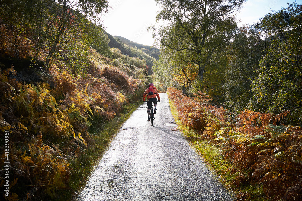 Male mountain biker biking on rural road, rear view, Achnasheen, Scottish Highlands, Scotland Male mountain biker biking on rural road, rear view, Achnasheen, Scottish Highlands, Scotland
