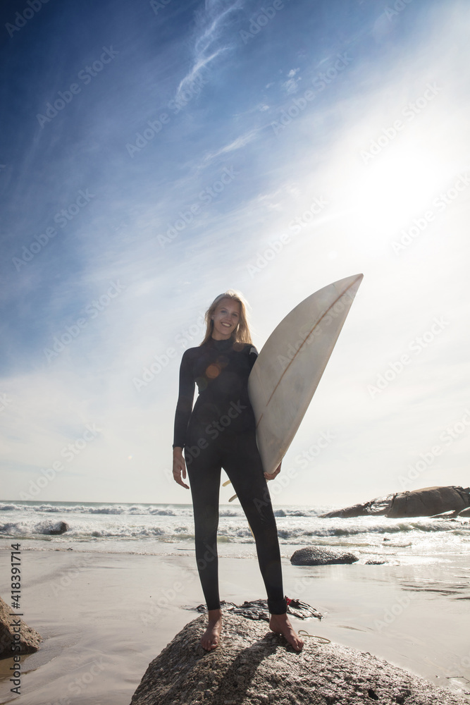 Young female surfer carrying surfboard on beach rock, full length ...