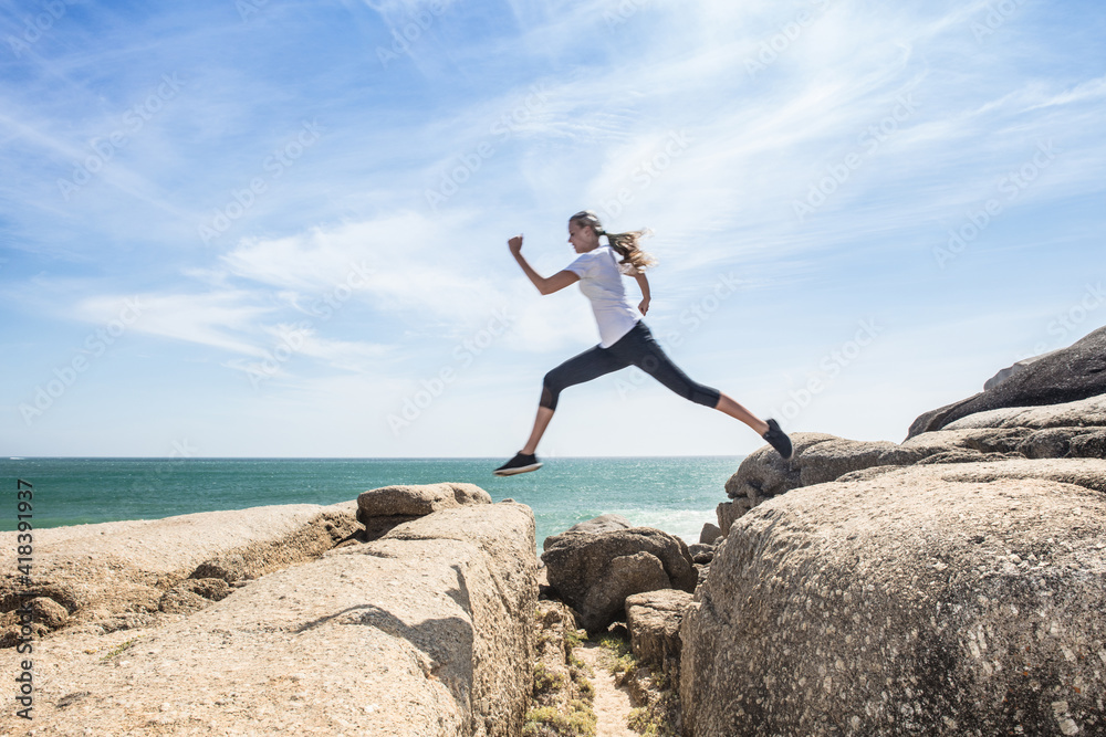 Young female runner leaping over beach rocks, full length, Cape Town, Western Cape, South Africa Young female runner leaping over beach rocks, full length, Cape Town, Western Cape, South Africa