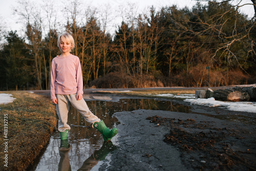 Boy standing ankle deep in rural meltwater puddle, portrait photo