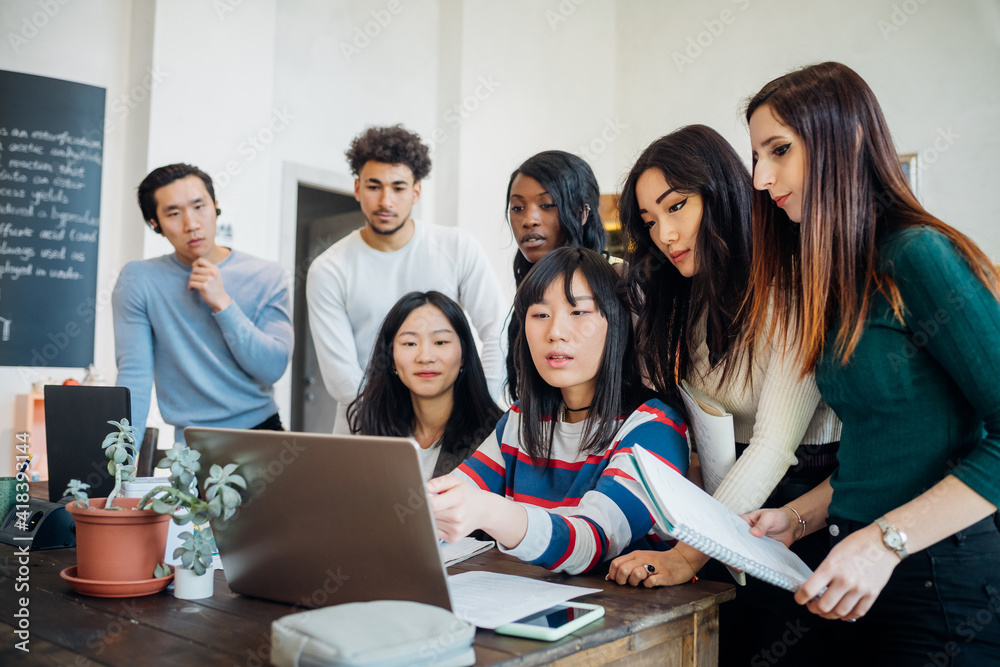Group of young businesswomen and men looking at laptop in office meeting Group of young businesswomen and men looking at laptop in office meeting