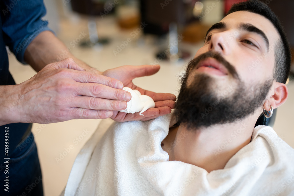 Hairdresser preparing to shave customer's beard in barber shop