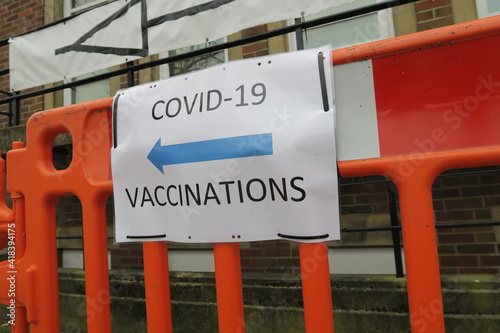 Covid-19 Vaccination signs to Vaccination clinic this way with blue arrow. Homemade signage found in the UK suburbs, DIY notice tells public which way to go for help during the coronavirus pandemic 