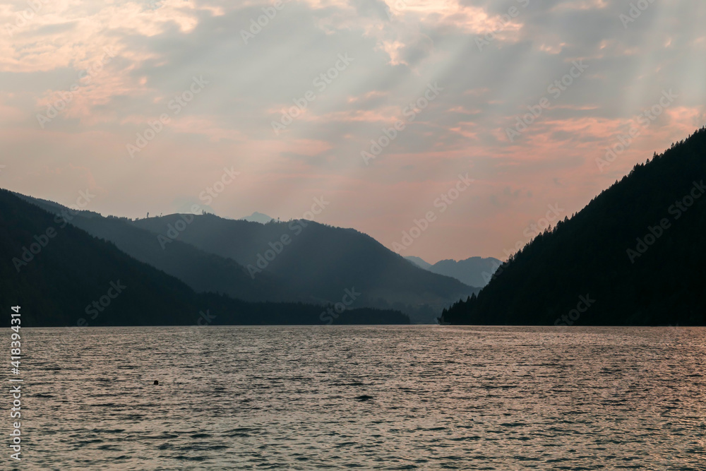 An early morning at the Weissensee lake in Austria. The sky is bursting with orange. The lake is surrounded by high Alps. Endless chains of mountains. Serenity and peacefulness. Day break An early morning at the Weissensee lake in Austria. The sky is bursting with orange. The lake is surrounded by high Alps. Endless chains of mountains. Serenity and peacefulness. Day break