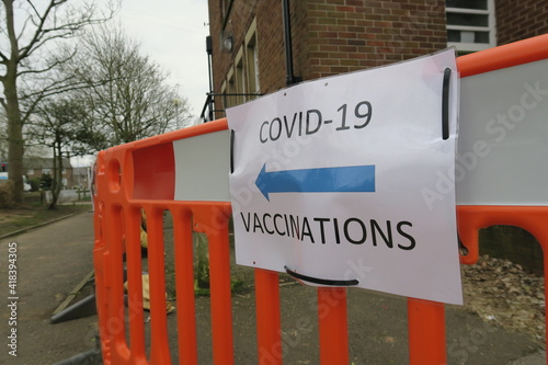 Covid-19 Vaccination signs to Vaccination clinic this way with blue arrow. Homemade signage found in the UK suburbs, DIY notice tells public which way to go for help during the coronavirus pandemic 