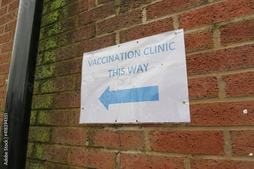 Covid-19 Vaccination signs to Vaccination clinic this way with blue arrow. Homemade signage found in the UK suburbs, DIY notice tells public which way to go for help during the coronavirus pandemic 