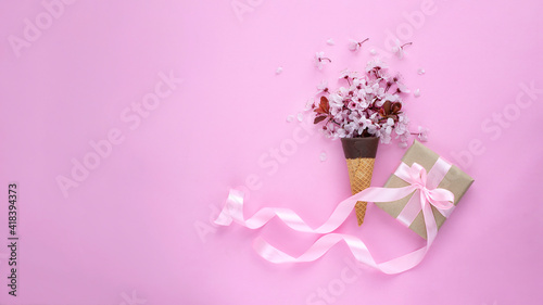 Cherry blossom in ice cream cone and gift box with pink ribbon on pink background. Web banner image with copy space