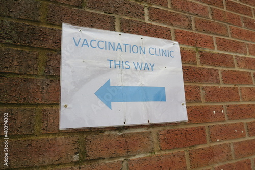 Covid-19 Vaccination signs to Vaccination clinic this way with blue arrow. Homemade signage found in the UK suburbs, DIY notice tells public which way to go for help during the coronavirus pandemic 