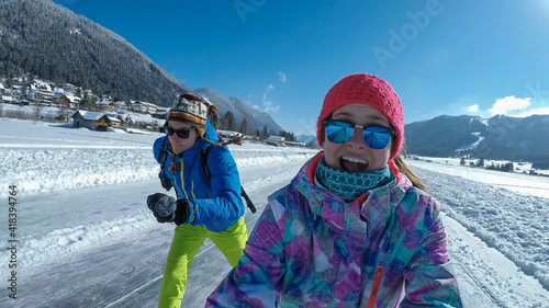 A couple in colorful outfits skating on a frozen Weissensee lake in Austria. The lake is surrounded by mountains. The ice rink is well prepared. Winter activity. Winter wonderland. Happiness and fun