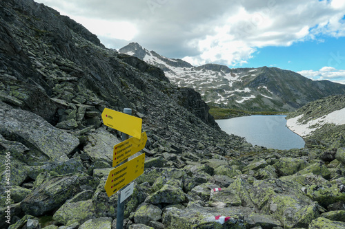 A sign leading to different destination in Maltal region in Austrian Alps. There is an artificial lake in the back. Summer in the mountains. Serenity and achievement. Choosing the way photo