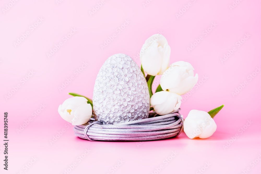 Grey easter egg in the nest and white tulips on a pink background Grey easter egg in the nest and white tulips on a pink background