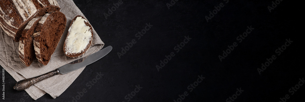 Freshly baked homemade artisan sourdough rye and white flour bread. Sliced. Bread and butter and vintage table knife on dark background. Banner. Copy space.